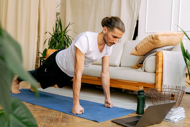 A man practices yoga while looking at a laptop screen.
