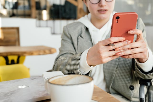 A woman with a mug of coffee types on her cell phone.
