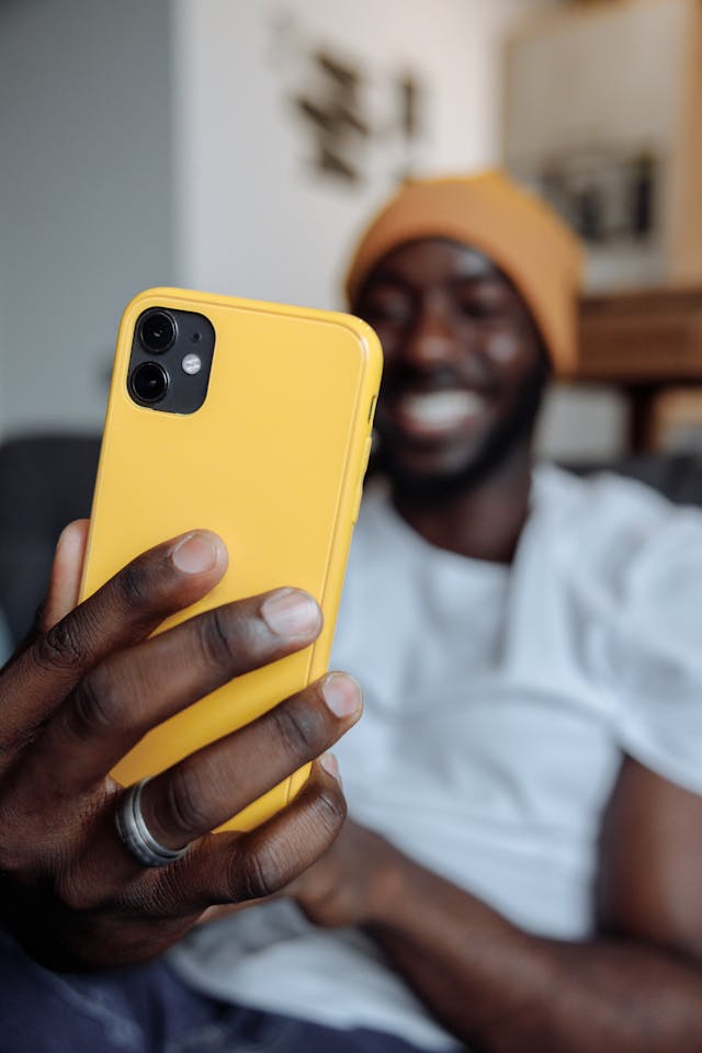 A man grins while holding a phone with a yellow case.
