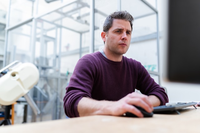 A man looks confused as he uses his mouse to browse on his computer. 
