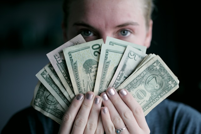 A person holds a fan of U.S. dollar bills in front of their face. 
