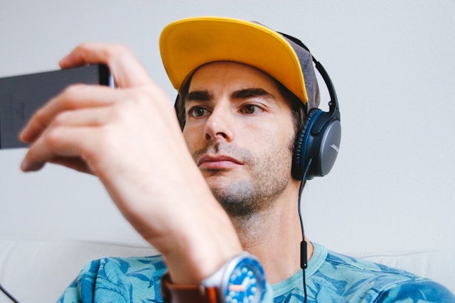 A man wearing a cap and headphones watches TikTok videos on his phone. 
