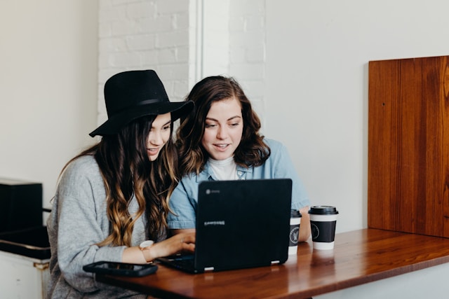 Two women edit videos together using a laptop. 
