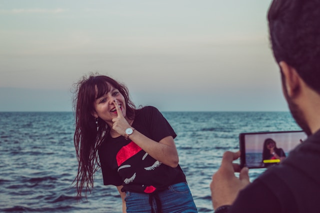 A man takes a video of a woman making funny faces at the camera. 
