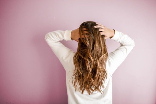 A woman in a white sweater faces the wall and has her hands in her hair. 
