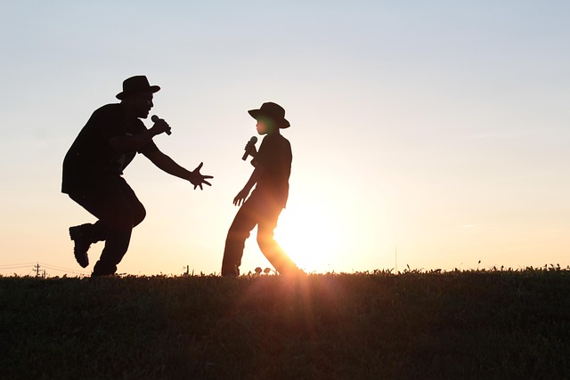 Two people sing with microphones while the sun sets behind them.
