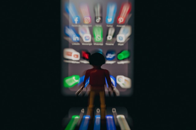 A figurine on a blurry phone screen displaying several social media apps.
