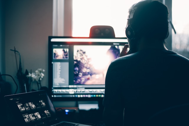 Ein Mann bearbeitet ein Video mit seinem Laptop und seinem Desktop-Computer.