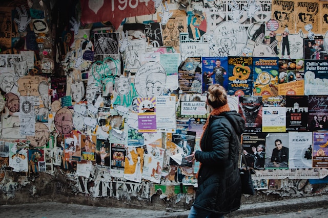 A woman looks at a wall covered with printed ads.
