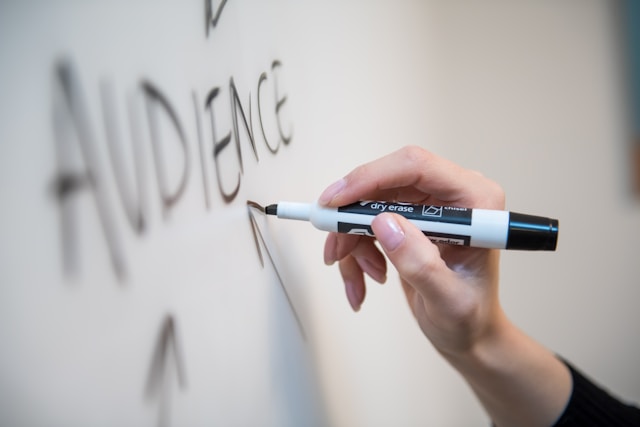 Someone writes the word "AUDIENCE" on a whiteboard using a pen.
