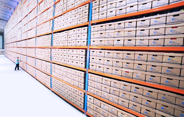 A person browses stacked cardboard file boxes in a huge warehouse. 
