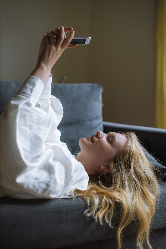 A woman lies on her back with her phone above her head.
