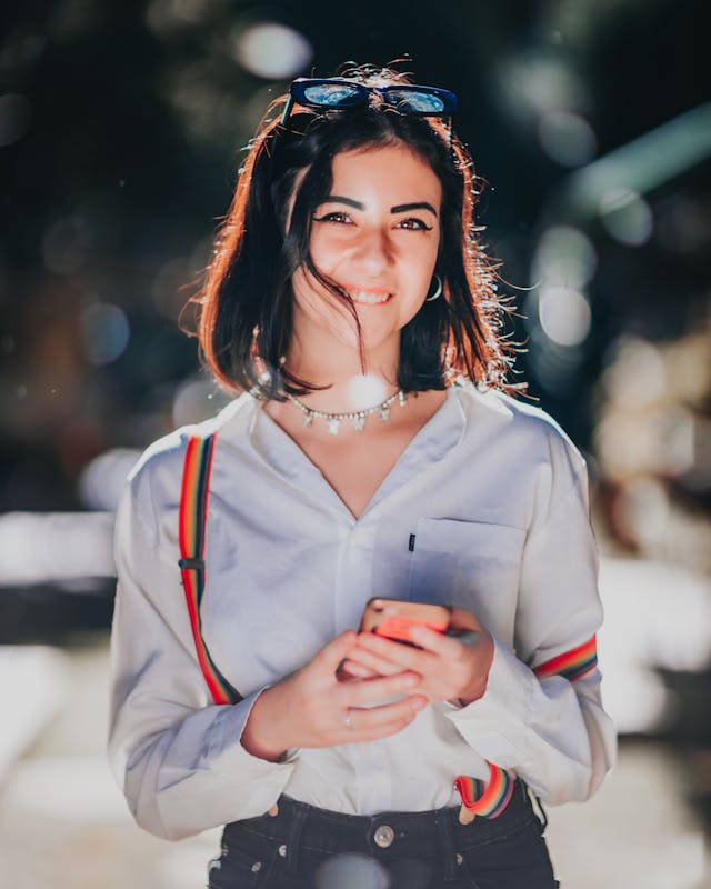 A woman grins as she holds her phone with both hands.
