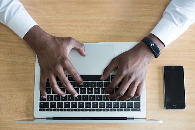 Aerial view of a man’s hands typing on a laptop.
