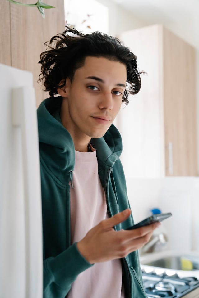 A man in a green hoodie casually uses his phone.
