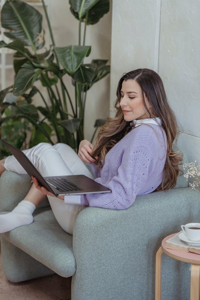 A woman in a purple sweater looks down at her laptop.
