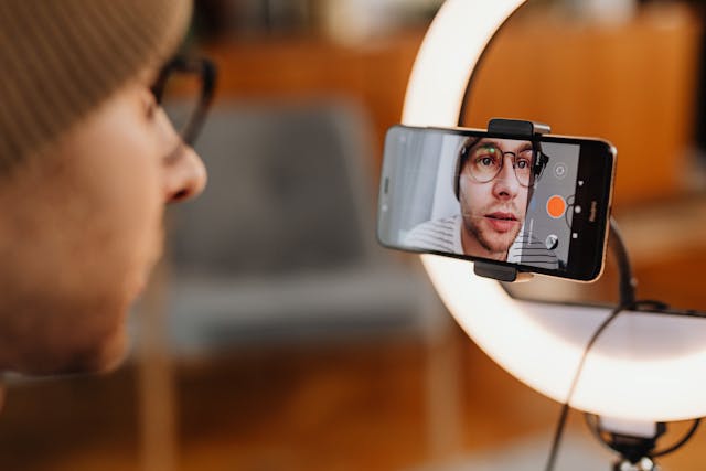 A man records a video in front of a ring light.
