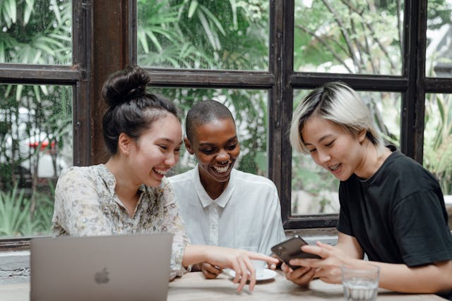 A diverse group of women look at a phone screen.
