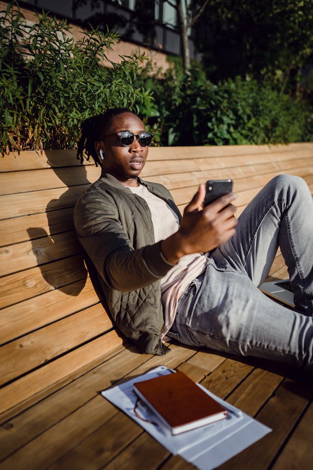 A man with sunglasses uses his phone while on a bench.
