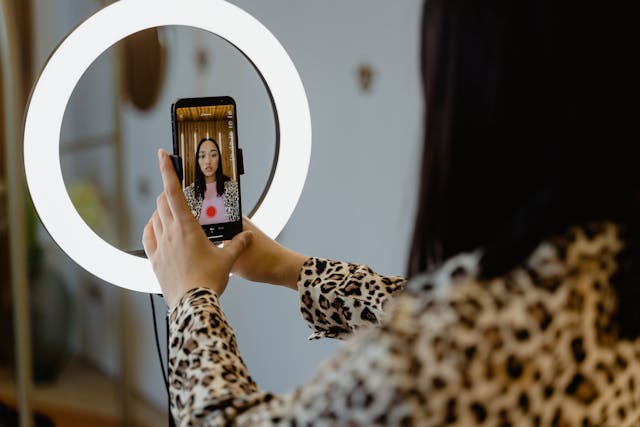 A person records themself on a mobile device before a ring light.
