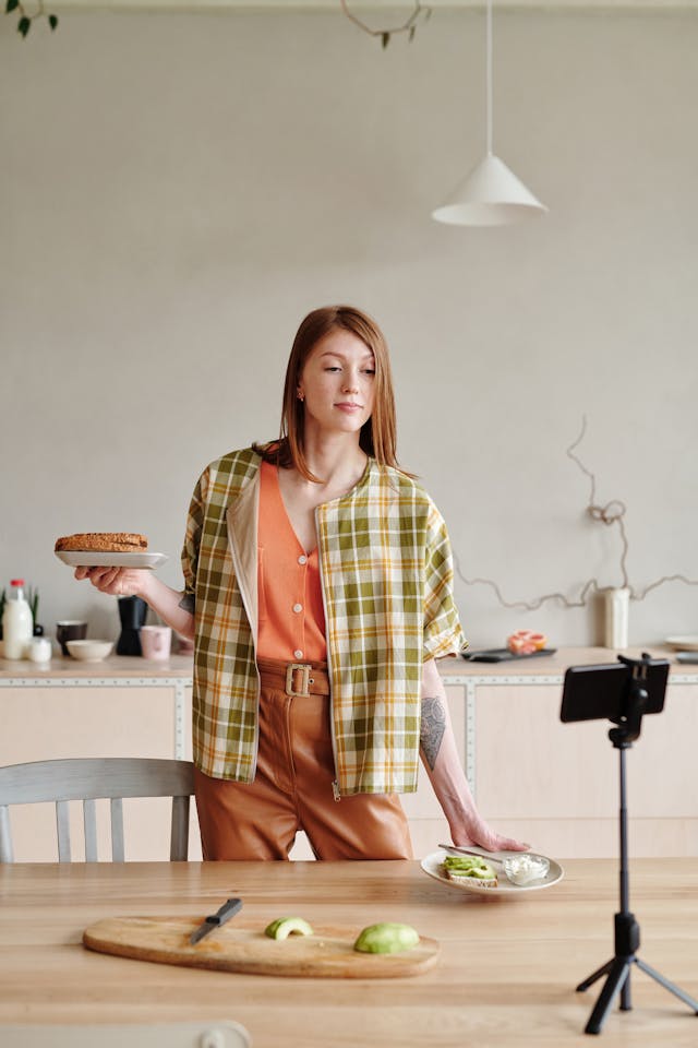 A woman records herself in a kitchen with food.
