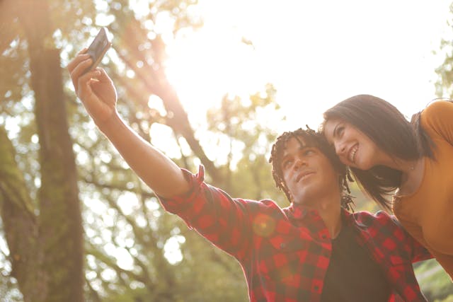 Two people take a selfie using a cell phone.
