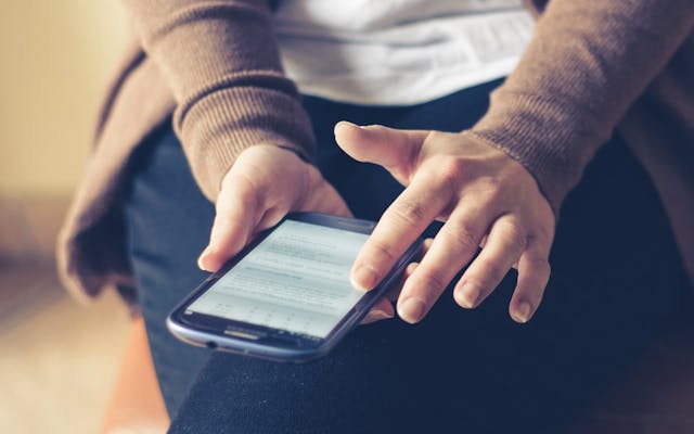 A person’s hands in their lap swipe across a phone screen.
