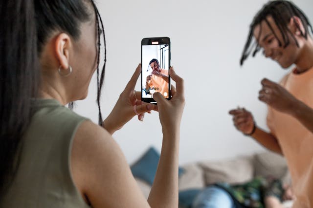 A woman records a man while he performs.
