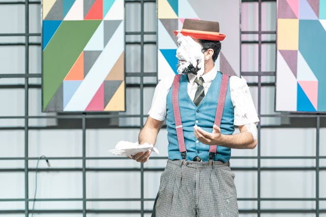 A comedian performs on a stage with cake on their face.
