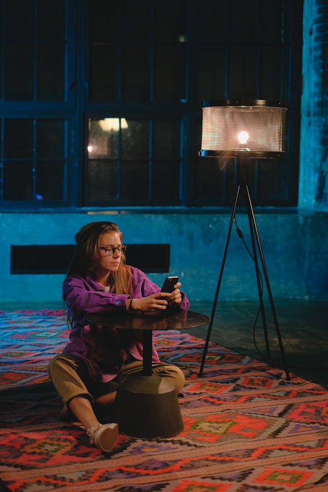 A woman uses her phone on the floor of a dimly lit room.
