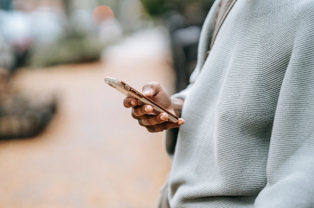 A person in a sweater uses one hand to type on a phone.
