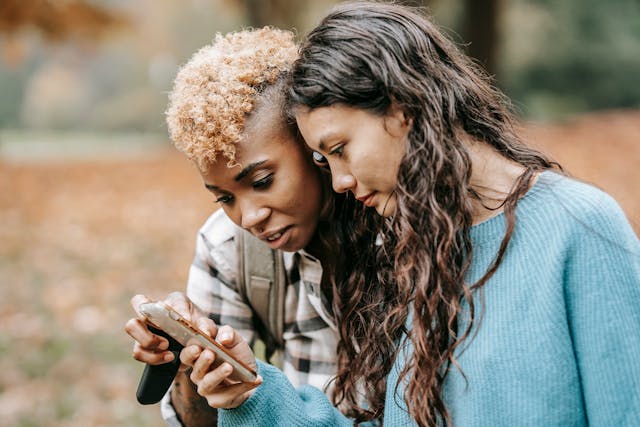 Two women stare intently at a phone screen.
