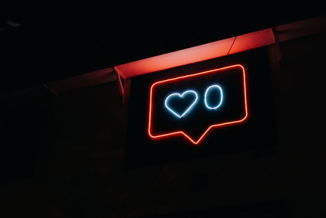 A neon sign with the shape of a like button hangs on a wall.
