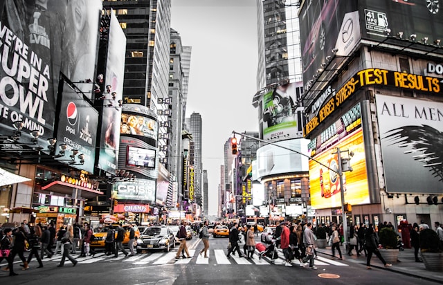 Pedestrians cross a busy street with digital ads looming on the sides of buildings. 
