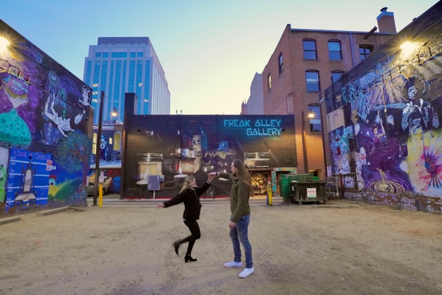 A couple dances in front of concrete walls filled with graffiti. 
