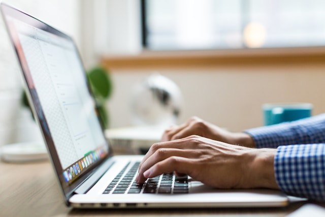 A man sits on a table and types on his laptop. 
