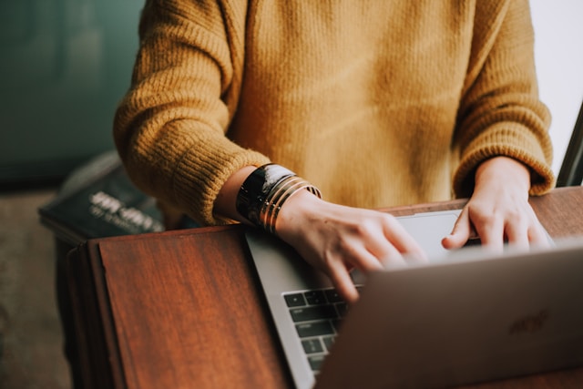 A person sits on a work table and types on their laptop. 
