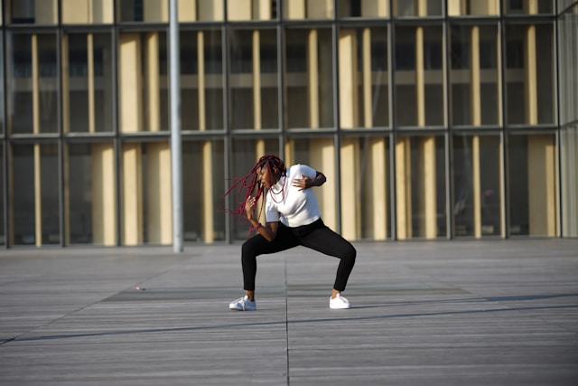 A woman whips her long, red dreadlocks as she dances in front of a building. 