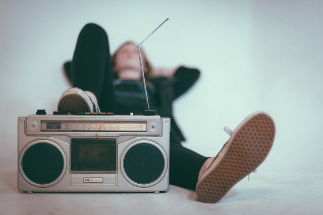 A person is lying down as they listen to music from an old-fashioned radio. 
