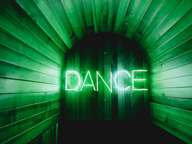 A lighted sign on a wooden wall reads, “Dance.”
