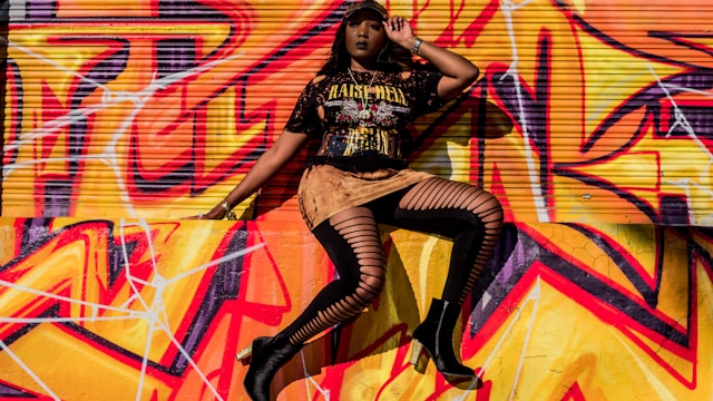 A female model poses in front of a concrete wall covered with red, orange, and yellow graffiti. 
