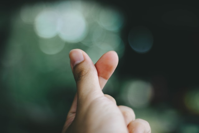 A person puts their thumb across their index finger to make a finger heart. 