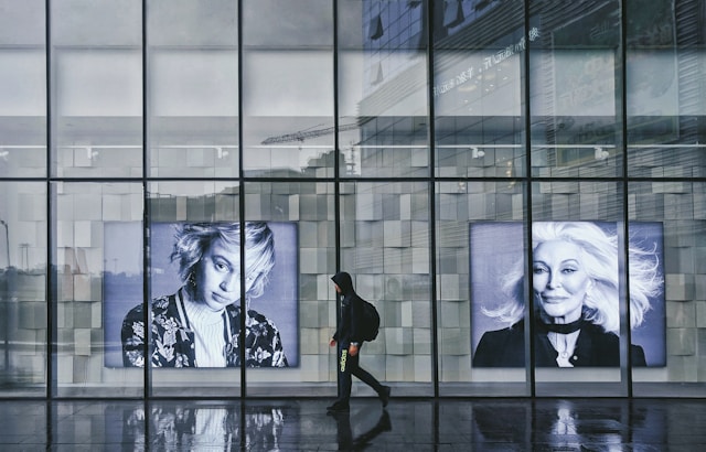 A person walks in front of a giant glass window display showing two female models representing two different age groups. 