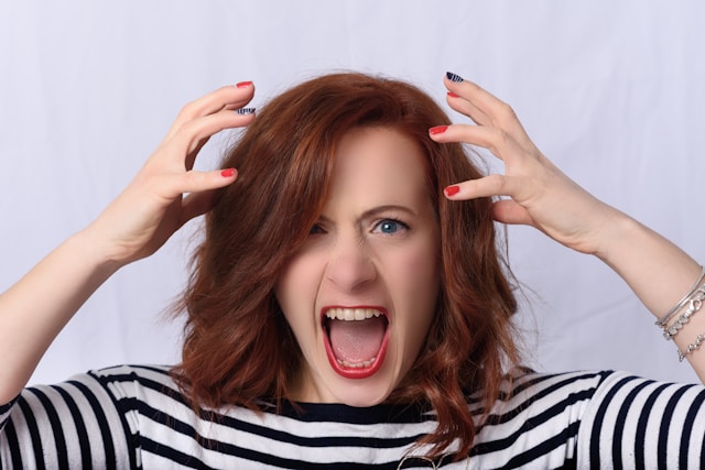 A woman’s hands hover over her head as she screams in frustration. 