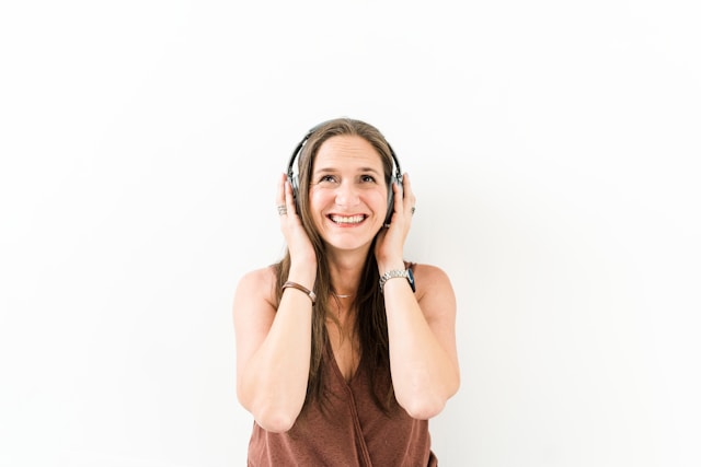 A woman wearing headphones has a big smile as she listens to music. 
