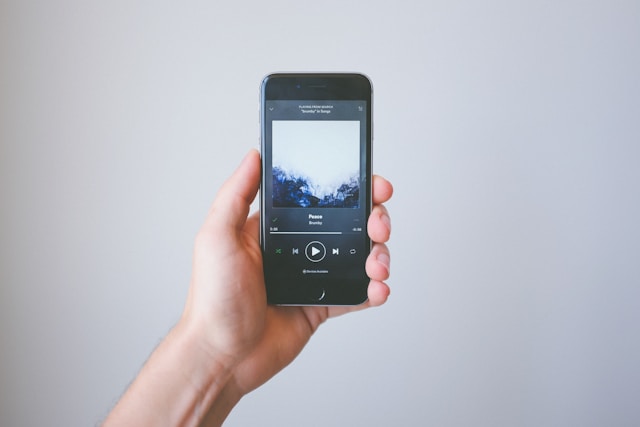 A person’s hand holds up a phone as it plays music. 
