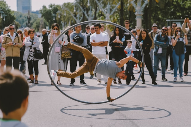 An audience gathers around a man performing acrobatics on the street. 
