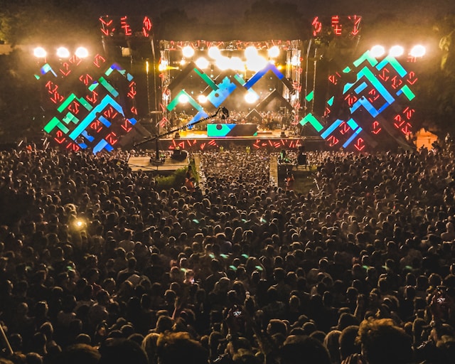 A massive crowd gathers in front of a stage and waits for the live performance to start.