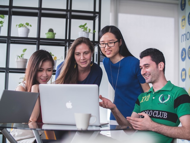 A business team gathers around a laptop. 
