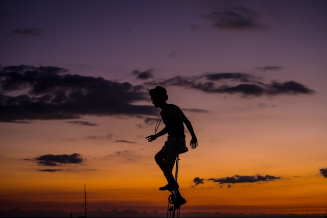 A silhouette of a man riding a unicycle with the sunset in the background. 
